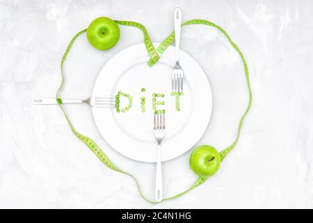 Plat créatif de la mention DIÈTE faite de pois verts sur plaque blanche, trois fourchettes, deux pommes et un ruban de mesure doux enveloppé en forme d'un son Banque D'Images