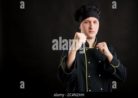 Portrait d'un jeune homme vêtu d'un costume de chef noir montrant des poings, boxe posant sur un fond noir isolé avec espace de copie publicitaire Banque D'Images