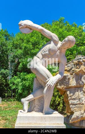 Ciel bleu extérieur, arbre vert et sculpture de lanceur de discus, sculpteur grec Myron fabriqué autour de 450 av. J.-C. Banque D'Images