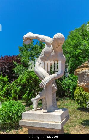 Ciel bleu extérieur, arbre vert et sculpture de lanceur de discus, sculpteur grec Myron fabriqué autour de 450 av. J.-C. Banque D'Images