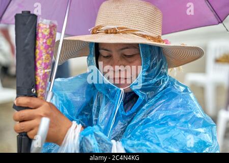 Une dame sous la pluie portant un imperméable et portant un parapluie. Banque D'Images