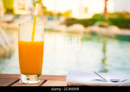 Vue rapprochée ensoleillée d'un verre de jus de mangue frais sur une table près de la piscine Banque D'Images