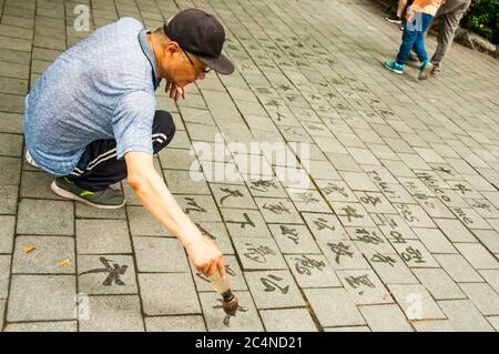 Un vieil homme écrit de la calligraphie à l’aide d’une brosse à eau dans le parc lu Xun de Shanghai. Banque D'Images