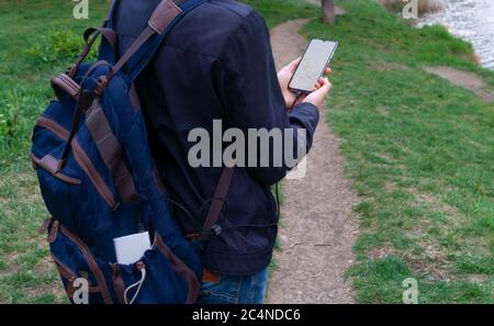 Homme tenant et utilisant un smartphone avec écran blanc vierge se recharge de la banque de puissance en extérieur avec un fond de nature Banque D'Images