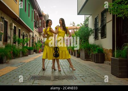 Deux belles sœurs jumelles violinistes dans des robes de concert jaunes posent avec des violons électriques sur la petite rue ottomane de la vieille ville d'Antalya Kalei Banque D'Images