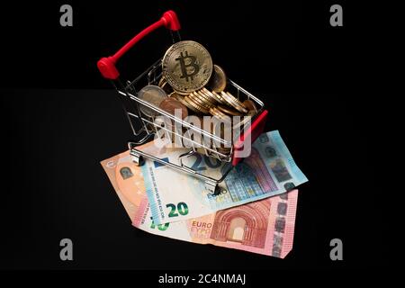 Panier miniature rempli de pièces en euros et d'un bitcoin sur le dessus placé sur l'argent papier avec un fond noir. Faire de l'argent crypto-monnaie. Banque D'Images