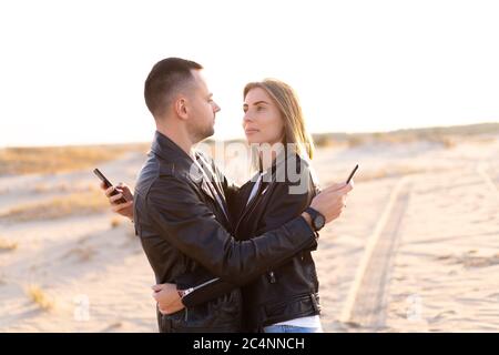 Heureux et mignon adorable adulte couple veste en cuir et jeans homme avec femme petite amie concept de marche sur la façon dont les téléphones mobiles réseaux sociaux et l'Internet affecte la relation entre les gens Banque D'Images