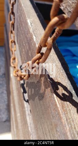 Gros plan de vieux maillons de chaîne en métal rouillé sur fond de bois de grunge en plein soleil avec des ombres sombres. Chaînes de protection vintage endommagées par la corrosion Banque D'Images