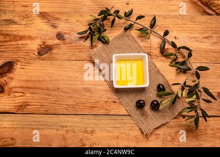 Vue de dessus à angle élevé de l'huile d'olive dans un plaque blanche à côté d'une branche d'olive sur un bois tableau Banque D'Images