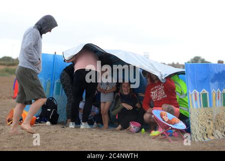 Une famille se protège du temps sur la plage de Skegness, car la pluie, le vent et les avertissements météorologiques ont mis fin à la vague de chaleur de juin. Banque D'Images