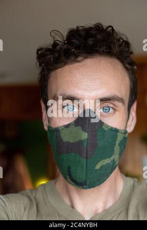 Jeune beau bleu-eyed homme dans le masque de tissu de camouflage regardant directement dans l'appareil photo Banque D'Images