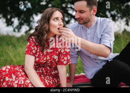 Jeune femme attirée avec un beau homme assis dehors sur une couverture rouge. Femme taske paille Banque D'Images