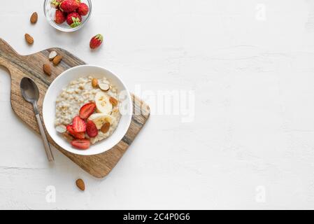 Porridge de flocons d'avoine avec fraises, amandes et banane dans un bol blanc. Petit déjeuner sain avec flocons d'avoine et baies fraîches bio, vue du dessus, espace copie. Banque D'Images