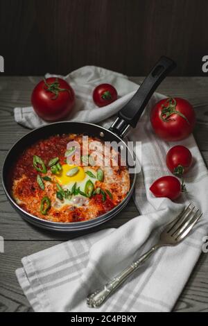 Shakshuka plat traditionnel moyen-oriental avec tomates et œufs dans une petite casserole garnie de gallium et de piment. Tomates en arrière-plan, sombres Banque D'Images