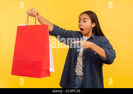 Portrait de l'excitée shopper fille dans le denim chemise pointant des sacs à l'air choqué, surpris par les achats fous dans la boutique de mode, thrift sale. indoo Banque D'Images