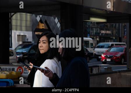 Photographie de rue de deux jeunes amies japonaises à Ginza. Station de métro, voitures et boutiques en arrière-plan. Tokyo, Japon. Banque D'Images