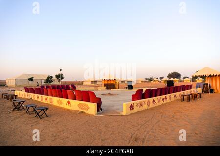 Vue en grand angle de la zone de divertissement et de sièges d'un camp dans le désert avec du sable autour et des tentes au loin Banque D'Images