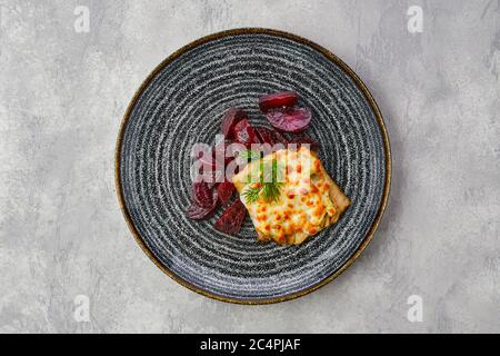 Vue de dessus du filet de morue frite avec garniture au fromage fondu et tranches de betteraves rôties sur fond de pierre râpe Banque D'Images