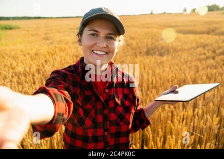 Une femme paysanne avec tablette numérique fait selfie sur le fond d'un champ de blé. Banque D'Images