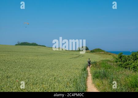 un cycliste suit un chemin de sable très étroit et un parapente vole à l'horizon Banque D'Images