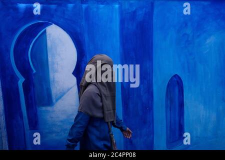 Une femme portant un niqab marche devant une murale décorée de bleu dans la médina antique. Chefchaouen. Djabala - région de RIF. Tanger - province de Tetuan. Nord Banque D'Images