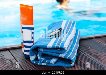 lunettes de soleil, tube de crème solaire, serviette bleue près de la piscine, fond tropical Banque D'Images