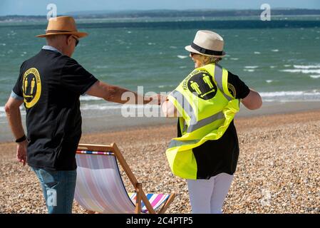 Southsea, Hampshire, Angleterre, Royaume-Uni. Juin 2020. Homme aidant la femme à porter un t-shirt social et à garder votre distance hi vis gilet Banque D'Images