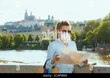 La vie pendant la pandémie de coronavirus. Élégante femme touristique solo dans un chemisier bleu avec masque médical, lunettes de soleil et carte touristique en plein air sur la ville str Banque D'Images