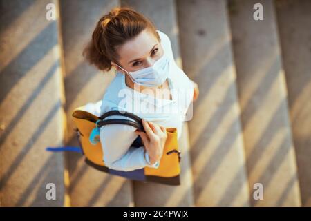 La vie durant la pandémie de Covid-19. Vue supérieure d'une élégante femme en blouse bleue avec masque médical, sac à main et assainisseur à l'extérieur de la ville. Banque D'Images