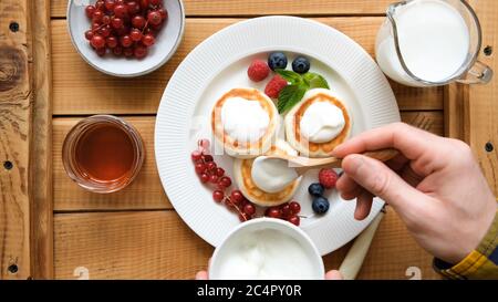 Beignets de fromage cottage servis avec des baies, du miel et de la crème aigre. Pour les hommes, garnir à la main de crêpes au fromage caillé fraîchement frites ou de syrniki avec de la crème aigre. À Banque D'Images