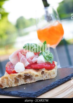 Tranche de pain de focaccia romana habillé de parme ha, de tomate, de mozzarella et de basilic frais. Verre de spritz italien sur fond Banque D'Images