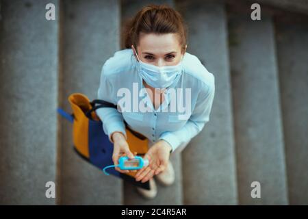 La vie durant la pandémie du coronavirus. Vue supérieure d'une femme de 40 ans en blouse bleue avec masque médical et sac à main désinfectant les mains avec un antibactérii Banque D'Images