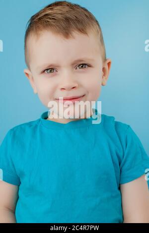 Portrait d'un petit garçon mignon avec une coiffure cury élégante en T-shirt bleu debout, regardant un appareil photo avec un visage attentif sérieux, expression pensive calme Banque D'Images