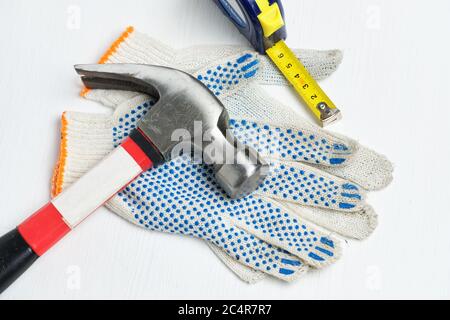 Marteau, mètre ruban sur gants de travail et fond en bois blanc. Banque D'Images