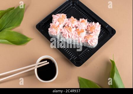 Petits pains à sushis recouverts de fromage à la crème rose et de crevettes. Petits pains à sushis placés dans des contenants en plastique noir. Livraison de nourriture asiatique. Arrière-plan beige Banque D'Images