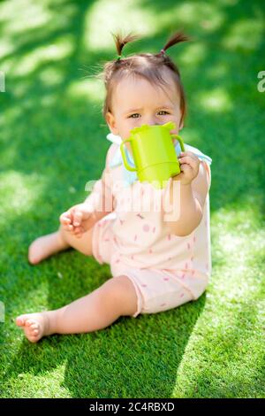 La petite fille boit de l'eau à partir d'une bouteille en plastique, en été sur l'herbe Banque D'Images