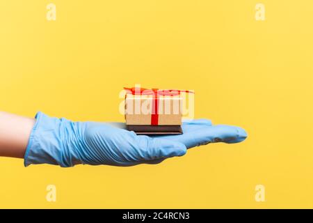 Vue latérale du profil gros plan de la main humaine dans des gants chirurgicaux bleus tenant une petite boîte cadeau. Partage, proposition de mariage, ou concept de livraison. Intérieur, Banque D'Images