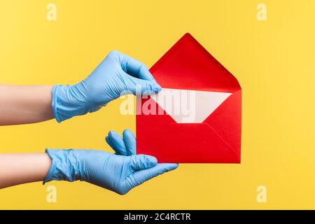 Vue latérale du profil gros plan de la main humaine en gants chirurgicaux bleus tenant la margelage de l'enveloppe rouge ouverte de lettre. Intérieur, studio, isolé sur yell Banque D'Images