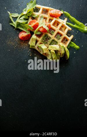 Gaufres belges fraîches avec arugula, tomates et avocat sur une assiette noire. Gaufres savoureuses. Concept petit déjeuner. Petit déjeuner sain Banque D'Images