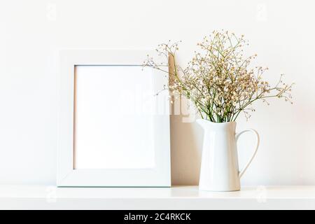 Cadre photo vierge et fleurs de Gypsophila dans un pot blanc, maquette. Banque D'Images