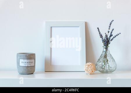 Cadre photo vierge à côté des fleurs de lavande dans un vase en verre et bougie parfumée, maquette. Banque D'Images