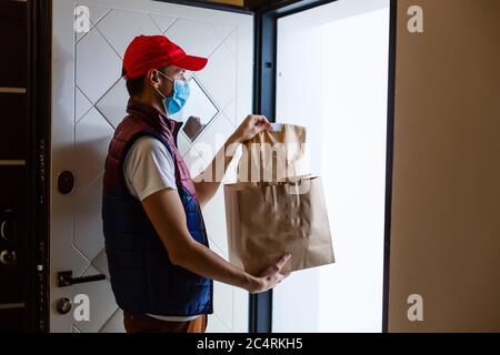 Liveur tenant un sac en papier avec des aliments sur fond blanc, liveur de nourriture dans un masque de protection Banque D'Images