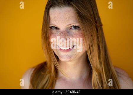 Gros plan sur une femme européenne souriante qui cherche un appareil photo. Femme à cheveux longs et sympathique sur fond jaune. Banque D'Images