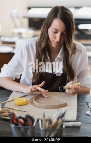 Gros plan d'un maître potter, outil spécial de coupe d'argile. Femme artiste coupant avec une boucle en bois Banque D'Images