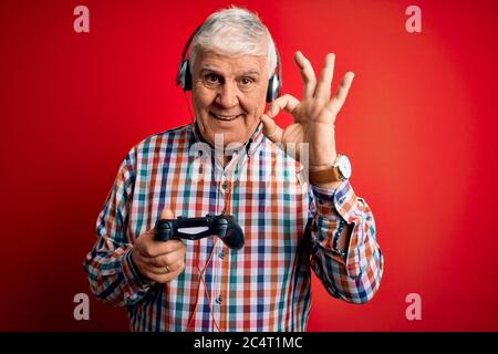 Senior beau joueur de hary homme jouant le jeu vidéo en utilisant le joystick et le casque faisant signe ok avec les doigts, excellent symbole Banque D'Images