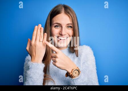 Jeune belle femme rouge portant l'anneau de mariage sur le doigt sur fond bleu très heureux pointant avec la main et le doigt Banque D'Images
