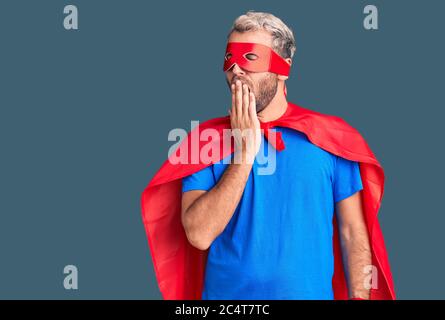 Jeune homme blond portant le super-héros crème s'ennuient, vêtu de la bouche, avec la main. Agité et somnolence. Banque D'Images