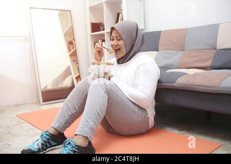 Femme asiatique musulmane portant hijab manger une nourriture saine, salade de légumes verts, après l'exercice à la maison, garder en bonne santé et en forme pendant le nouveau mode de vie normal co Banque D'Images