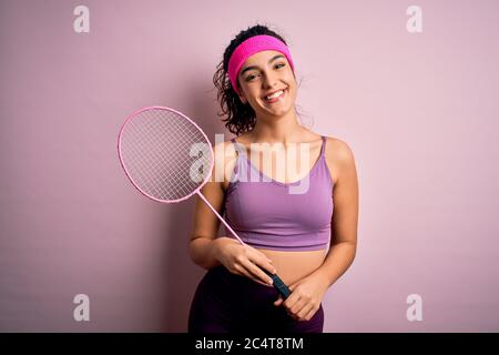 Belle sportswoman avec cheveux bouclés porter des vêtements de sport jouer au badminton uning raquette avec un visage heureux debout et souriant avec un sourire confiant Banque D'Images