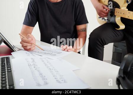 Compositeurs jouant de la guitare et écrivant des notes musicales sur des feuilles de papier lors de travaux sur une nouvelle chanson pour le groupe Banque D'Images